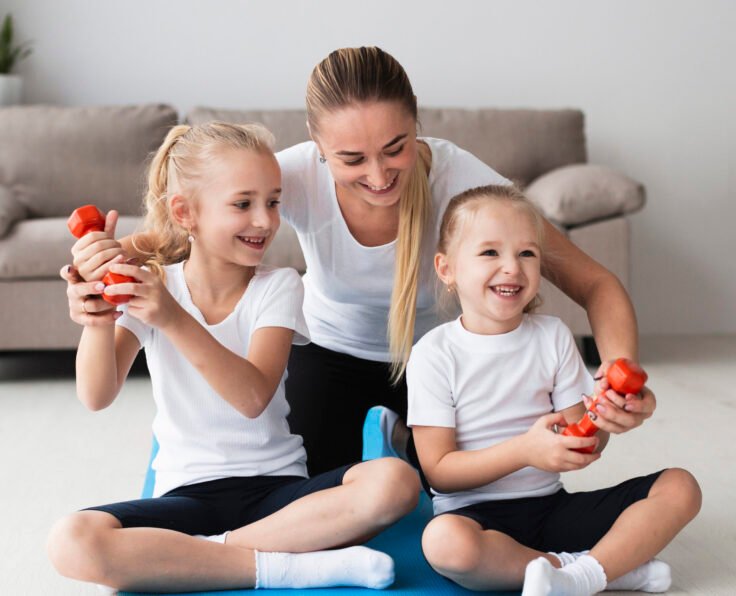 front-view-mother-posing-with-daughters-home-while-holding-weights